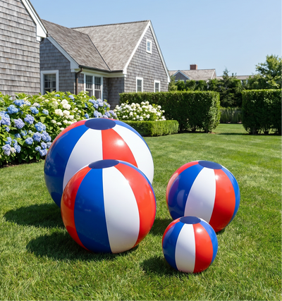 Set of red, white, and blue beach balls on a grassy lawn with a house in the background.