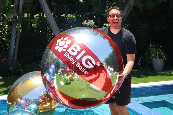 Person holding a large reflective sphere with 'BIG' branding by a poolside.