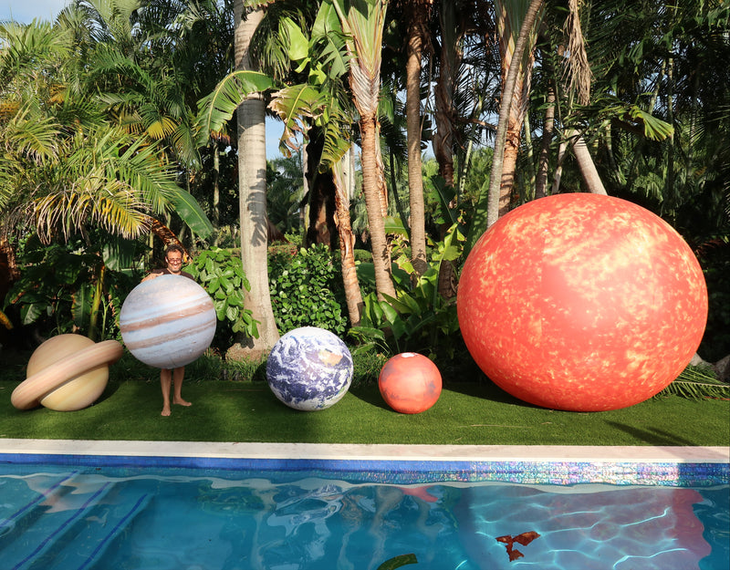 Giant inflatable planet models by a pool with a tropical background