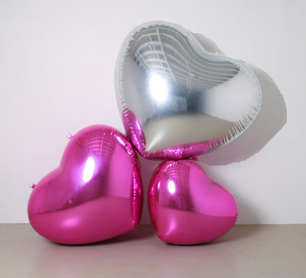 Two heart-shaped balloons, one pink and one silver, on a plain background.