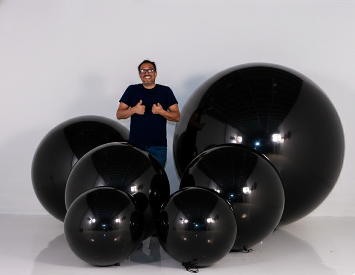 Man standing among large black balloons on a white background