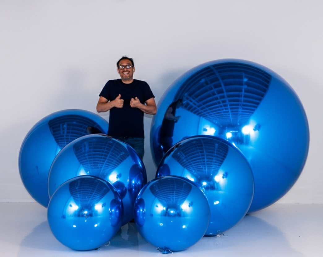 Person standing next to large blue reflective spheres on a white background