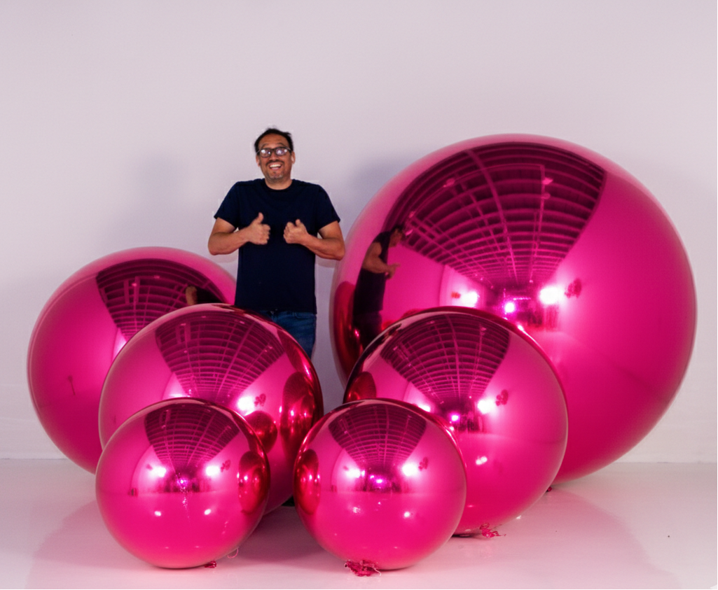Person standing next to large pink reflective spheres on a white background