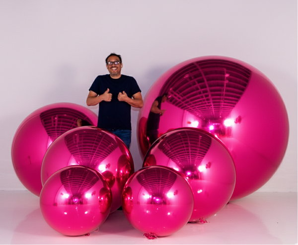 Person standing next to large pink reflective spheres on a white background