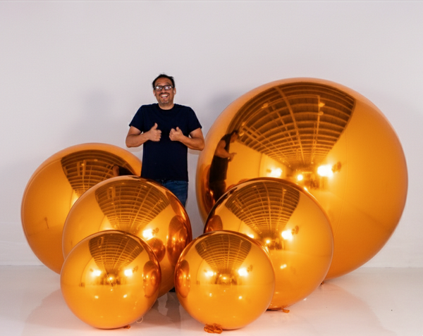 Man standing next to large metallic gold spheres on a white background