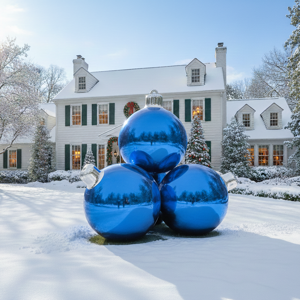 Large blue Christmas ornaments in front of a snow-covered house with festive lights.