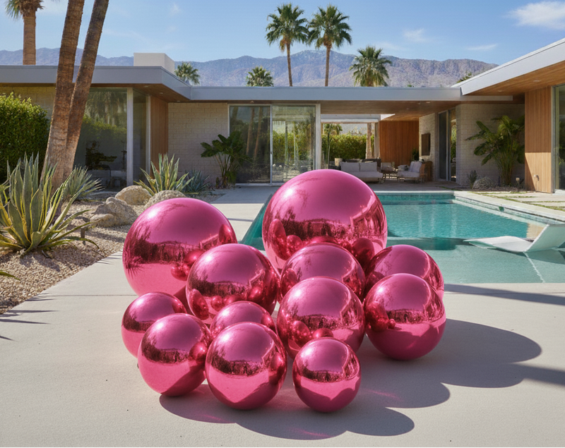 Pink reflective spheres in front of a modern house with a pool and palm trees.
