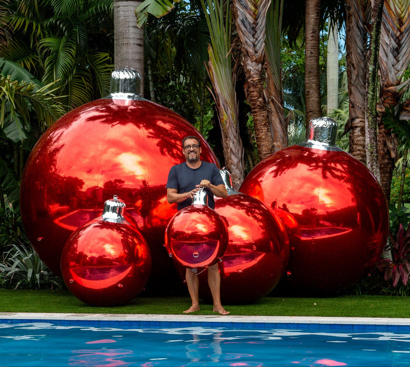 Giant red chrome inflatable Christmas ornaments in five sizes on a lawn by a pool for holiday party
