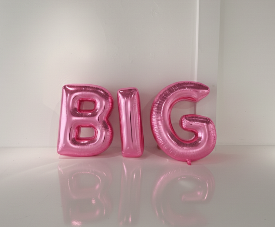 Pink 'BIG' letter balloons on a white surface with a white background