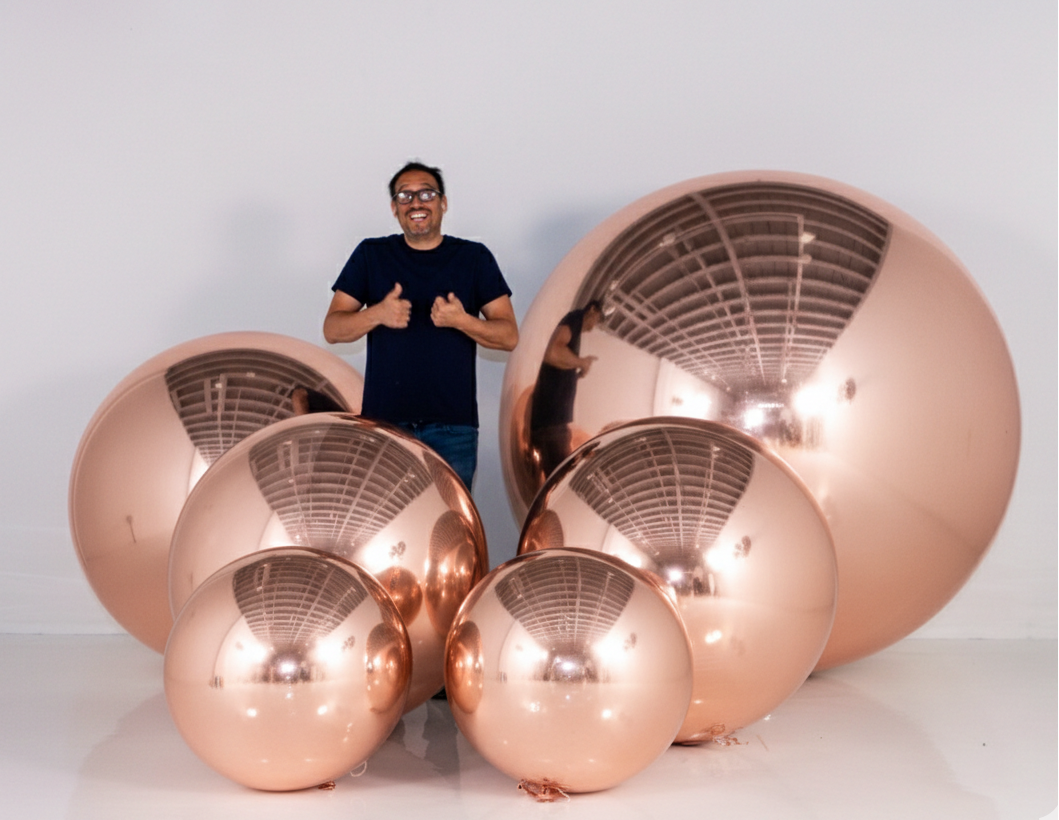 Person standing next to large copper spherical objects on a white background