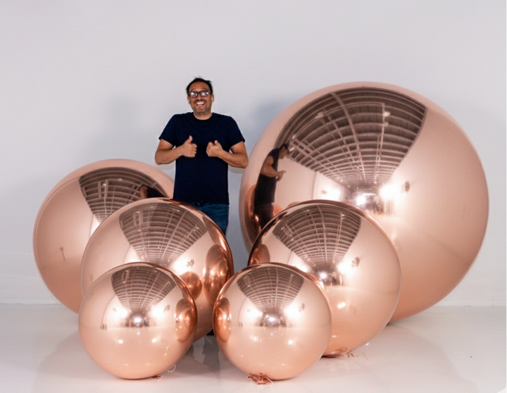 Person standing next to large copper spherical objects on a white background